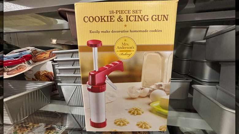 A box with a cookie and icing gun sits on a glass shelf in a store.