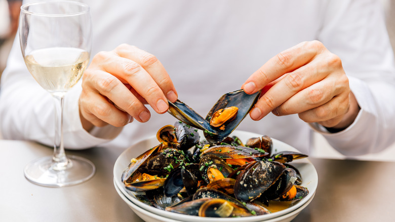 hands scraping mussel offa shell over a bowl of moules marinières