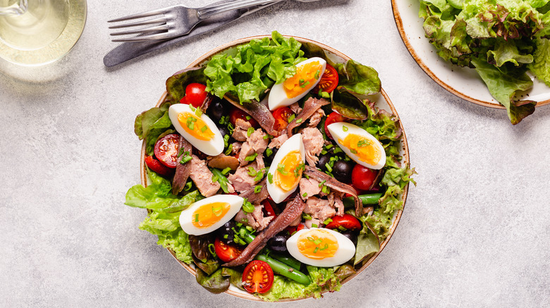 Bowl of salade Niçoise on speckled background with knife and fork