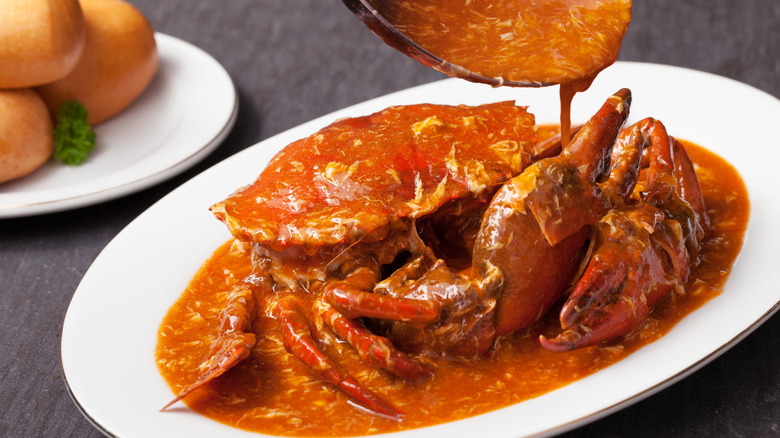 Plate of Singapore chili crab with sauce being poured from a ladle