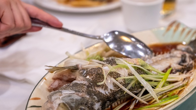 Steamed Chinese-style fish with ginger and scallions being served with a spoon
