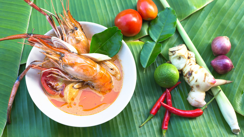 Bowl of Tom Yum Goong with large prawns in shell and ingredients alongside