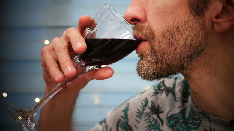 man holding glass of red wine by his mouth