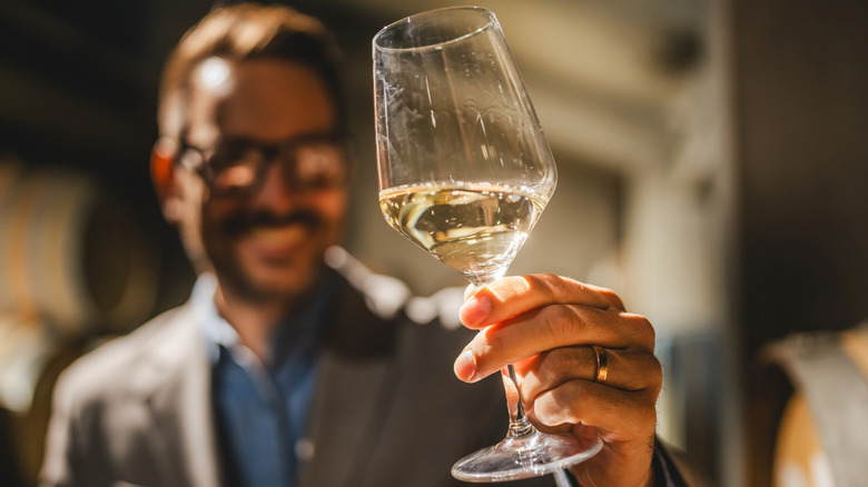 man smiling and looking at white wine in glass