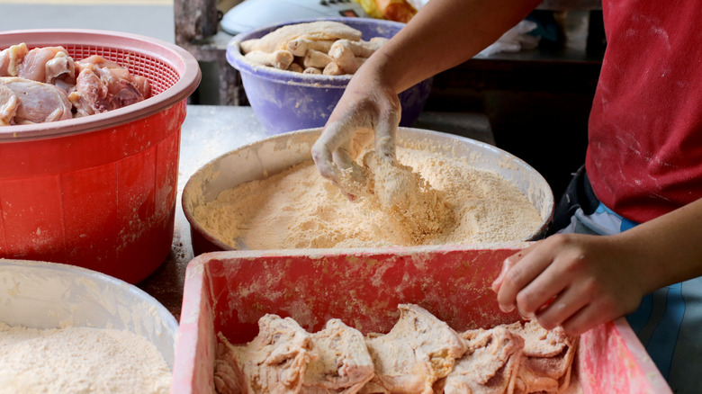 person dredging chicken in breadcrumbs