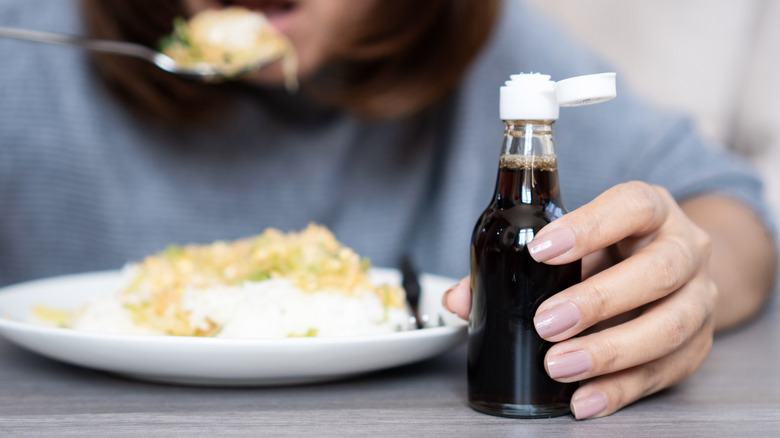 Woman holding a bottle of fish sauce as she eats in the background