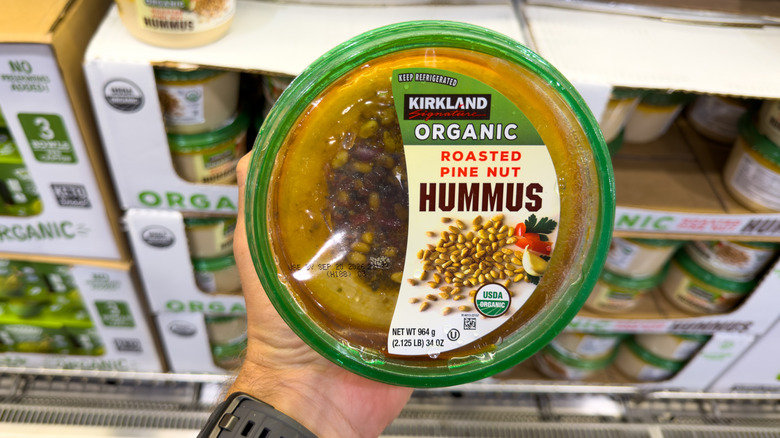 hand holding a tub of kirkland signature organic roasted pine nut hummus at costco