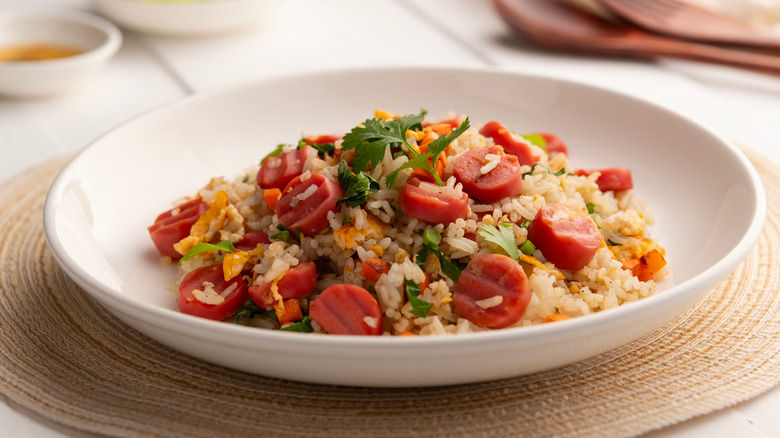 White bowl of fried rice with sliced hot dogs and vegetables
