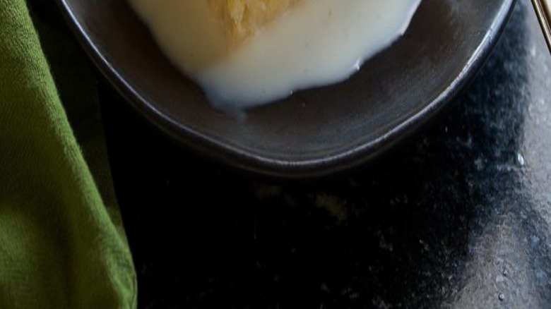 Tres leches cake on a black plate topped with a sliced strawberry