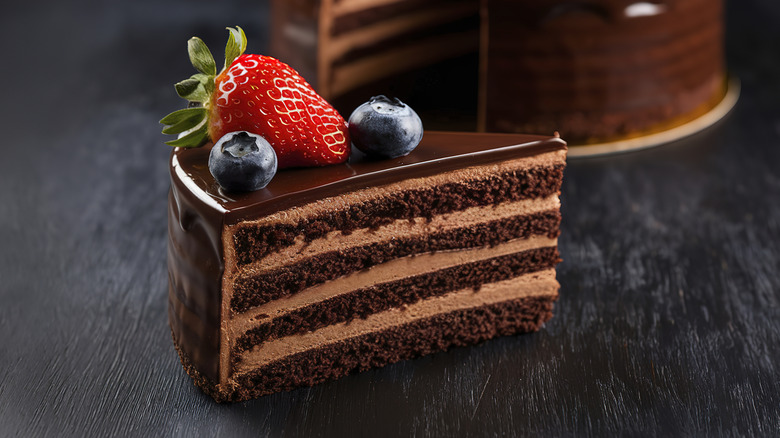 Devil's food cake garnished with two blueberries and a strawberry placed on a dark table
