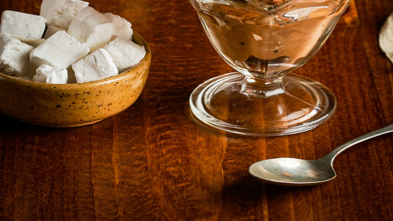 Rocky road ice cream in a glass next to marshmallows and an ice cream scoop on a wooden table