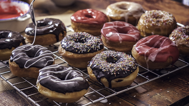 Doughnuts on a silver tray with a spoon in the air drizzling chocolate on a doughnut