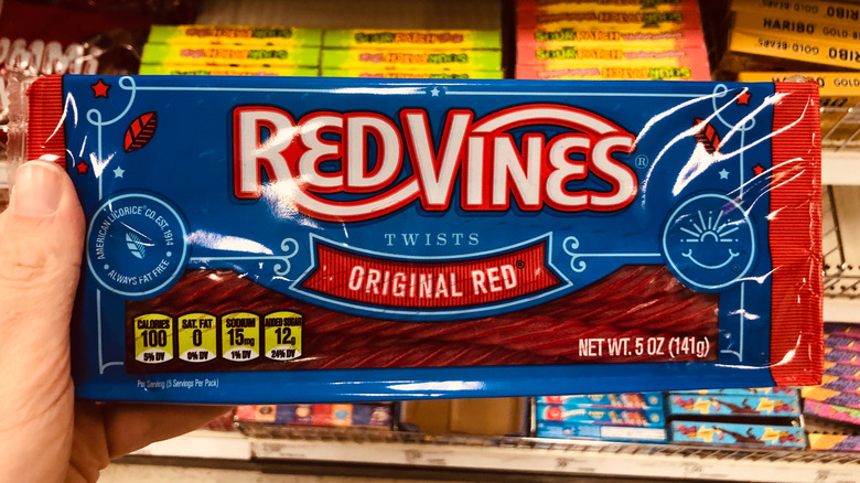 A hand holding a package of Red Vines Original Red candy