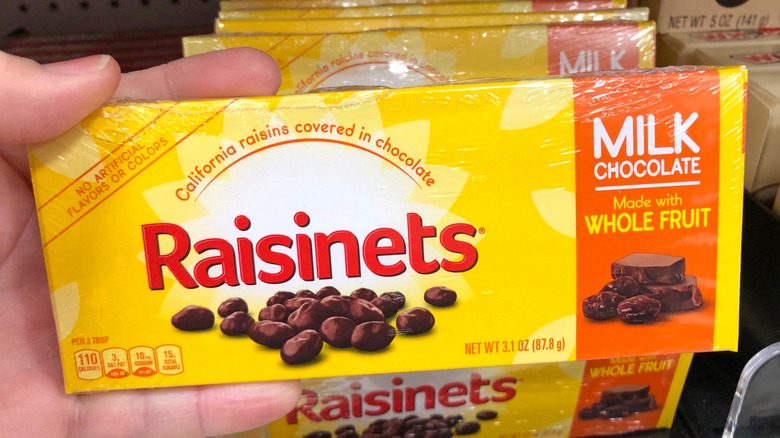 A hand holds up a box of Raisinets in front of a store display