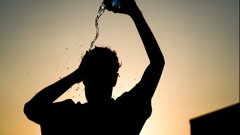 Silhouette of a person pouring water on themselves with the sun in the background.