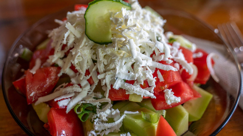 Shopska salad, cucumbers, tomatoes, and bell peppers topped with shredded feta cheese.