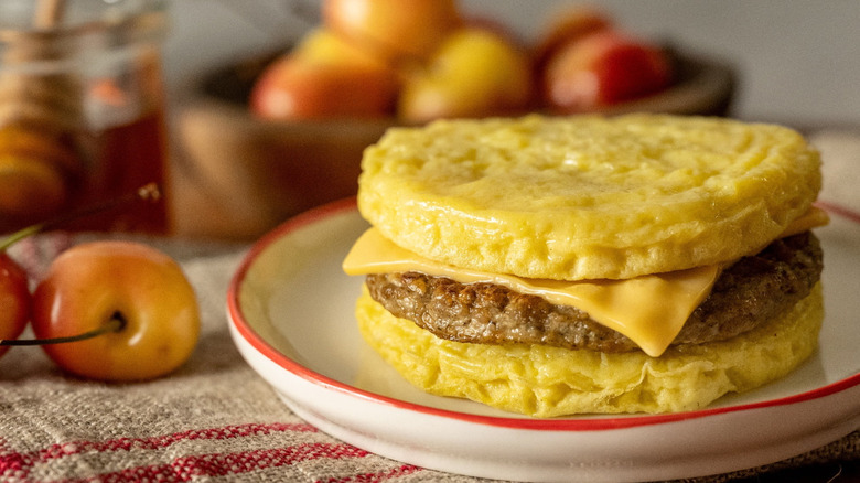 An Egg'Wich sandwich sits on a plate next to some cherries.
