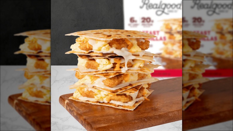 A stack of Realgood Foods Co. Breakfast Quesadillas sits on a wooden cutting board, with the product package in the background