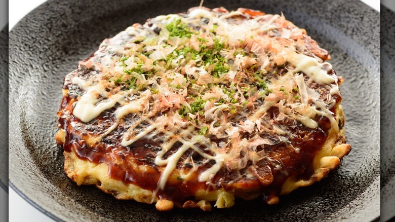 An Okonomiyaki sits on a dark plate.