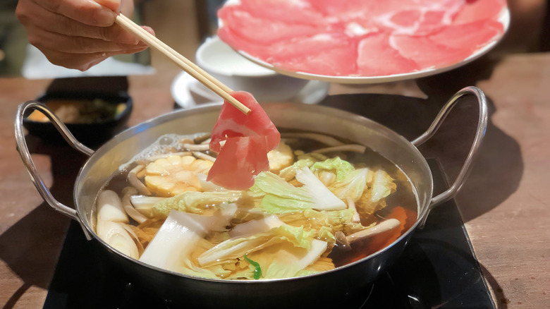 A person prepares to drop a piece of paper-thin pork into a shabu shabu pot