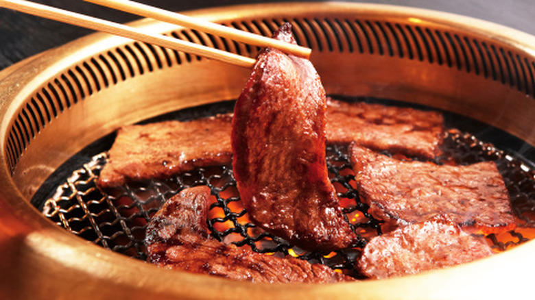 A person making yakiniku lifts a piece of beef from a small grill