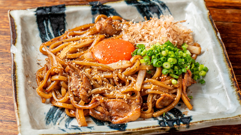A plate of yakisoba is topped with an egg yolk and scallion