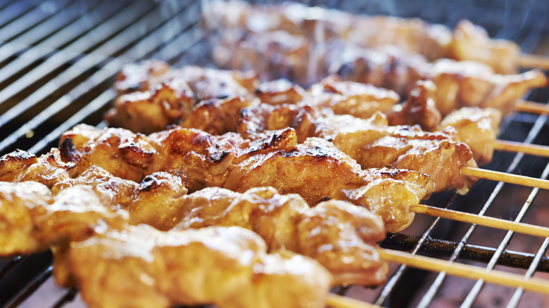 Yakitori skewers are being grilled on the grates of a grill.