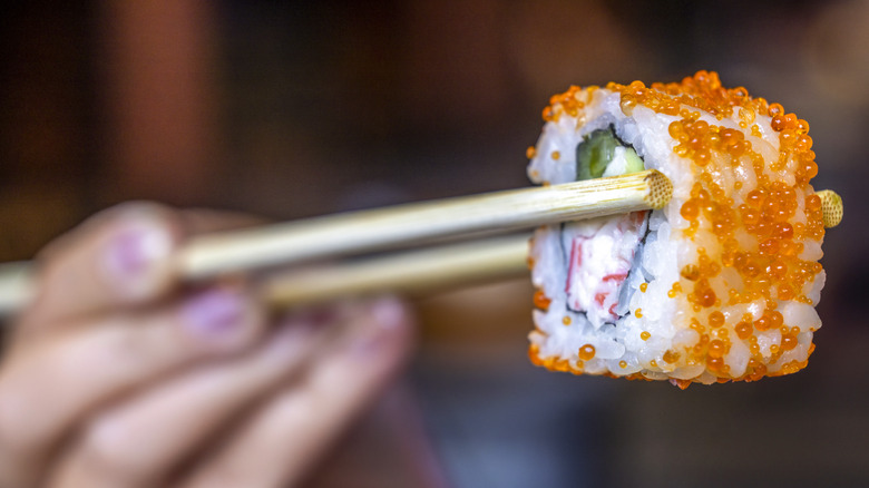 women holding sushi with chopsticks