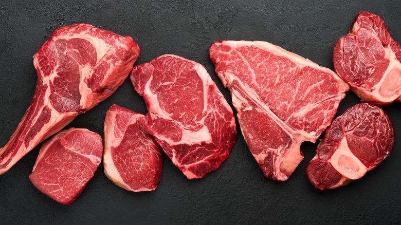 Different raw steak cuts on black board