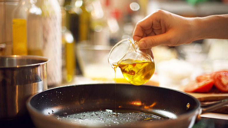 hand pouring small carafe of oil onto pan on stove