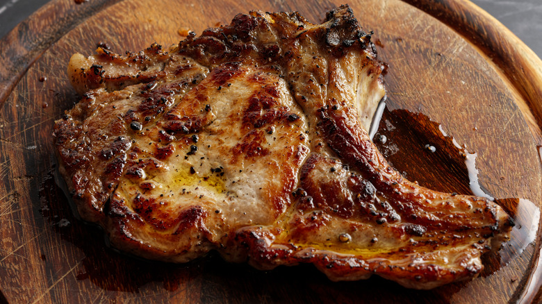 close up of cooked pork chop resting on cutting board with juices