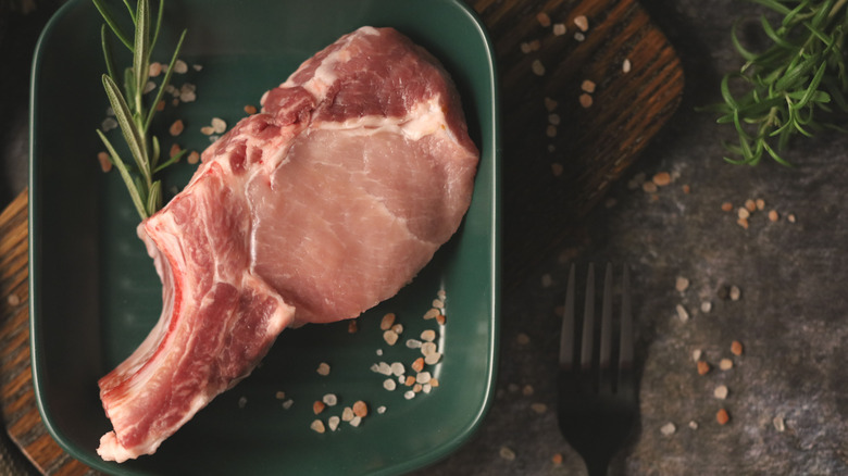 raw pork chop sitting on a green plate with herbs and salt