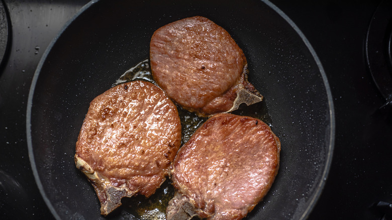 three pork chops close together cooking in pan