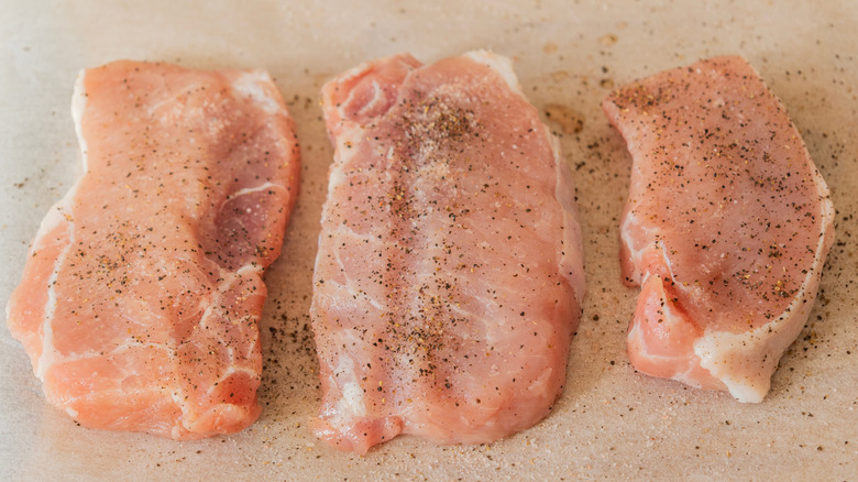 three raw pork chops on parchment with salt and pepper