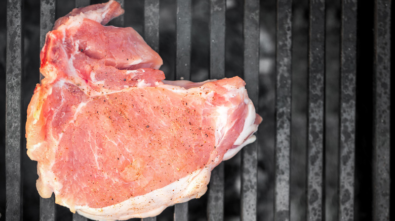 raw pork chop on grill grates with seasoning