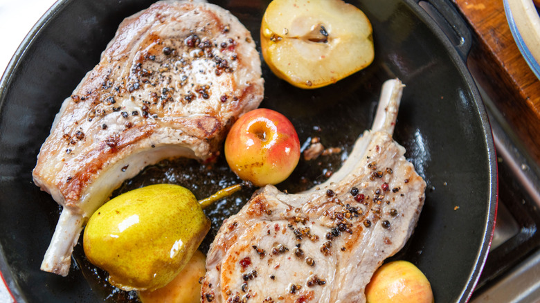 seasoned pork chops cooking in pan with sliced pears and apples