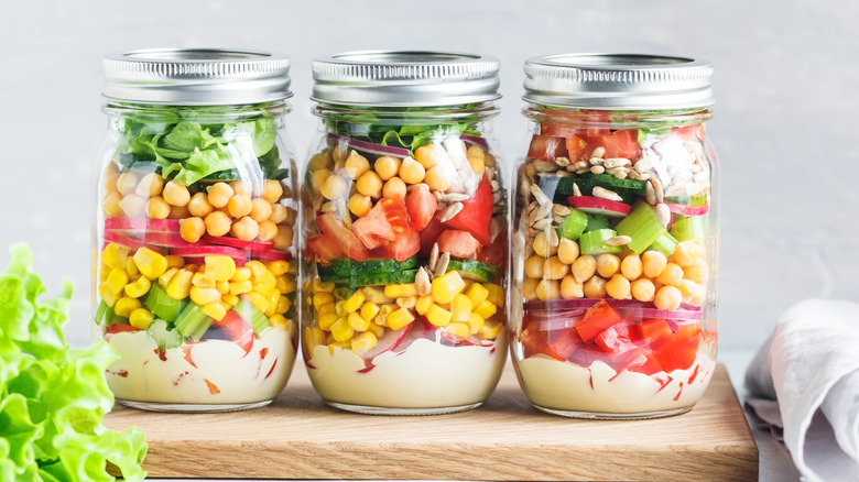Three jarred salads layered with dressing and vegetables