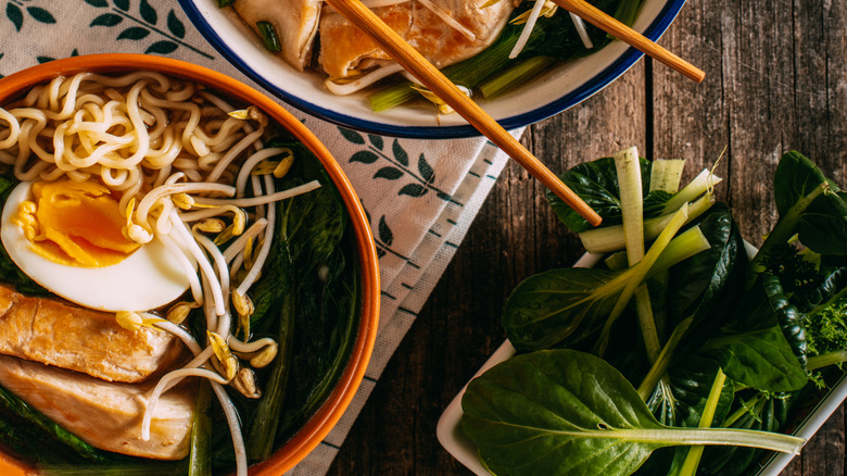 Chopsticks resting on a bowl of ramen atop a weathered table
