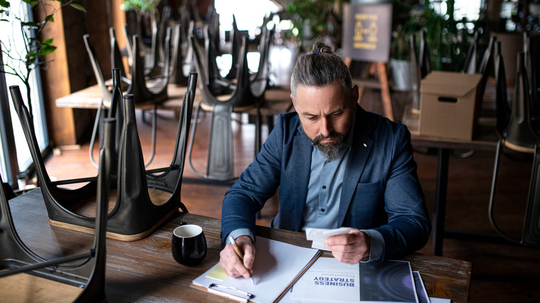 restaurant owner reviews strategy surrounded by chairs overturned on tables