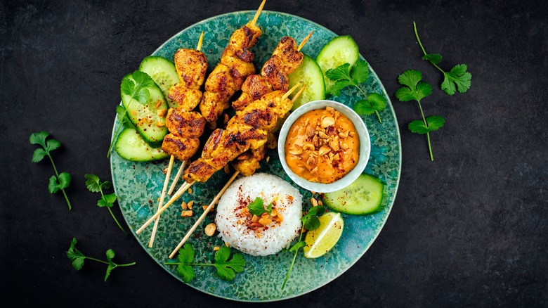 meat skewers, rice, and peanut sauce on a plate