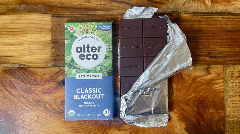 An unwrapped Alter Eco Classic Blackout 85% Cacao Dark Chocolate Bar lying on a wooden table top