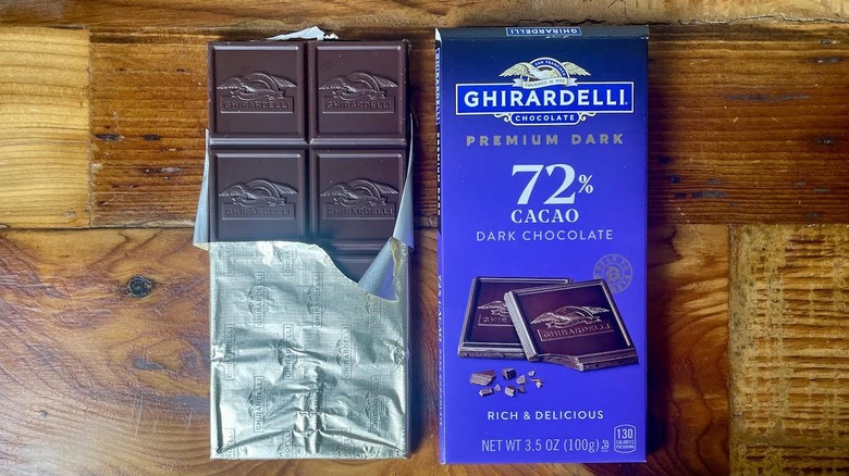 A partially unwrapped Ghirardelli Premium Dark 72% Cacao Dark Chocolate Bar lying on a wooden table top