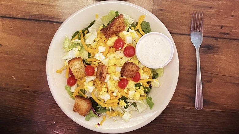 House salad topped with egg, cheese, croutons, and tomatoes on a wooden table