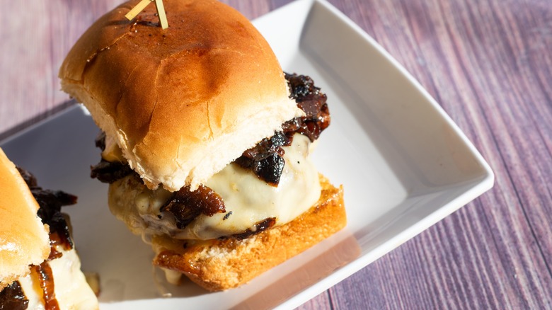 Close-up of a steak slider with cheese held together with a skewer on a platter
