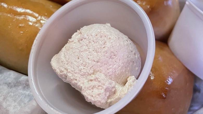 Container of Texas Roadhouse butter atop a pile of rolls