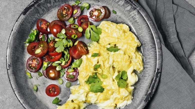 Plate of scrambled eggs with tomatoes and parsley