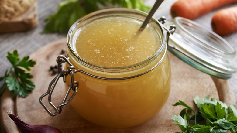 open jar filled with chicken stock on a circular wooden board