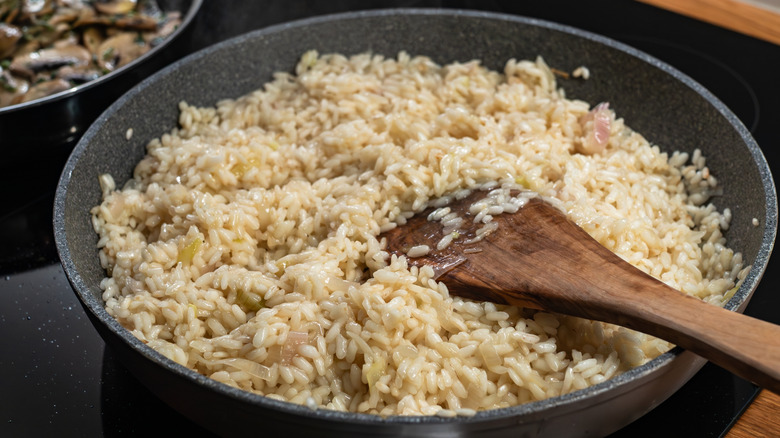 close up of a pan of risotto cooking on the stove with a wooden spoon in it
