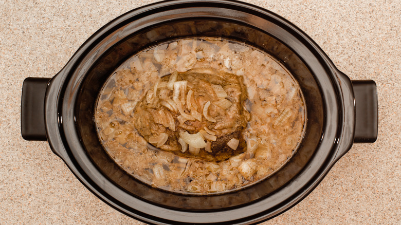 open slow cooker with a meat roast covered in onions and juices