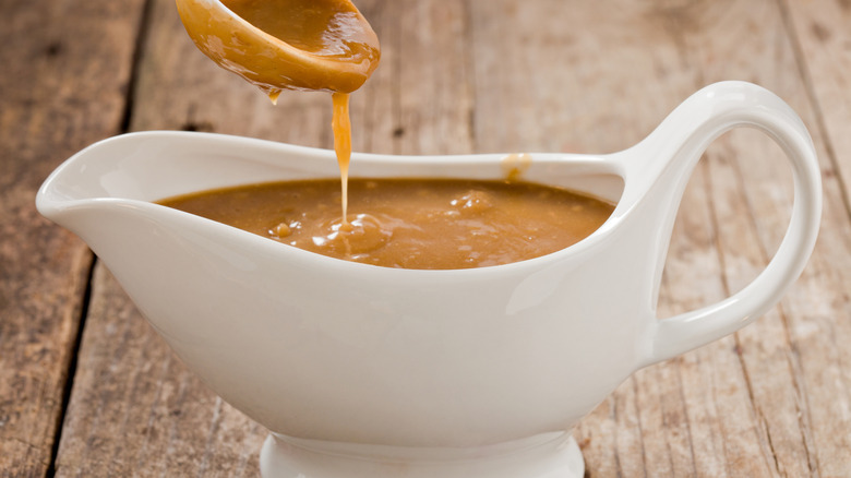 closeup of a gravy dish filled with gravy with a spoon dripping above it